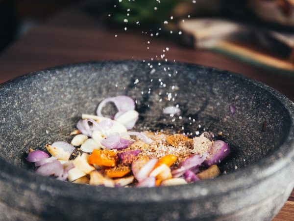Close-up of seasoning being added to fresh ingredients in a stone bowl, perfect for culinary themes.